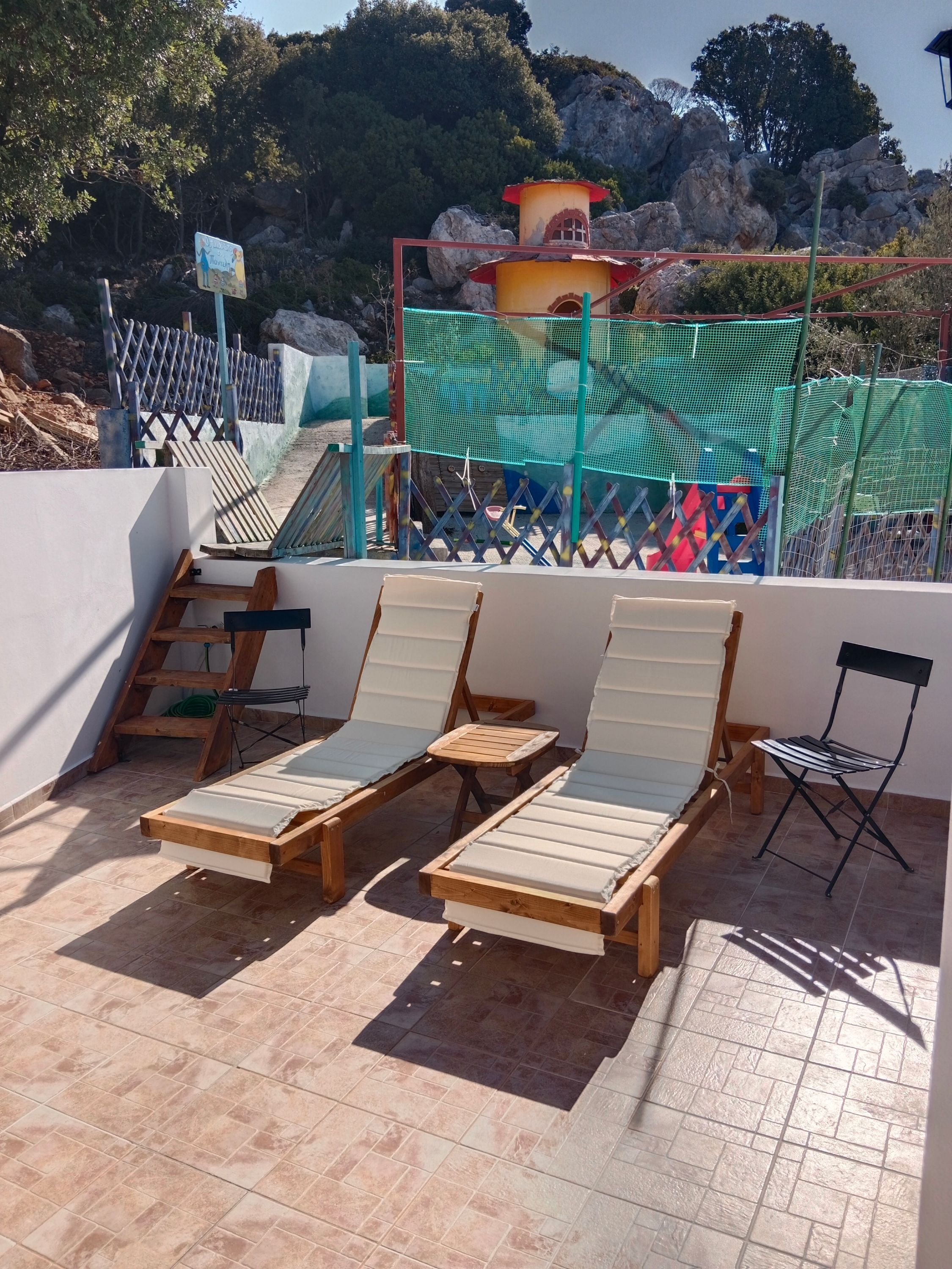A rooftop terrace with wooden lounge chairs and a view of a mountainous landscape.