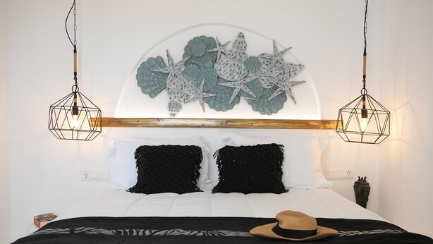 Quarto com cama, roupa de cama preta e branca, um objeto decorativo na parede e duas luminárias pendentes.