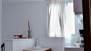 Uma cozinha pequena com bancada branca, mesa de madeira e janela com cortinas finas.