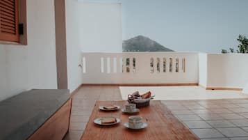 Un balcón con una mesa de madera dispuesta para el desayuno, un sofá y vistas a la montaña.