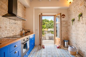 A kitchen with a stone wall, blue cabinets, and a view of a balcony. - Bee Tree Villa in Corfu (Corfu)