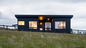 A modern, dark-colored building with large windows, a flat roof, and a fenced perimeter. - Barefoot Luxury, Romantic Escapes, Outdoor Bath with a view, Rolling hills (Carlton River)