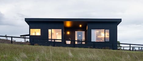 Un bâtiment moderne, de couleur sombre, doté de grandes fenêtres, d’un toit plat et d’un périmètre délimité par une clôture.