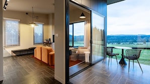 A modern interior with a sofa, a dining table with chairs, and a large sliding glass door leading to a balcony with a view of the countryside. - Barefoot Luxury, Romantic Escapes, Outdoor Bath with a view, Rolling hills (Carlton River)