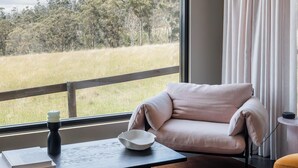 A room with a large window, a sofa, a table with a book and a candle, and a lamp. - Barefoot Luxury, Romantic Escapes, Outdoor Bath with a view, Rolling hills (Carlton River)