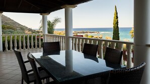 Uma área de refeições ao ar livre coberta, com vista para o mar e as colinas.