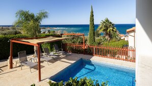 Uma área de piscina com pergolado, cadeiras de descanso e vista para o mar.