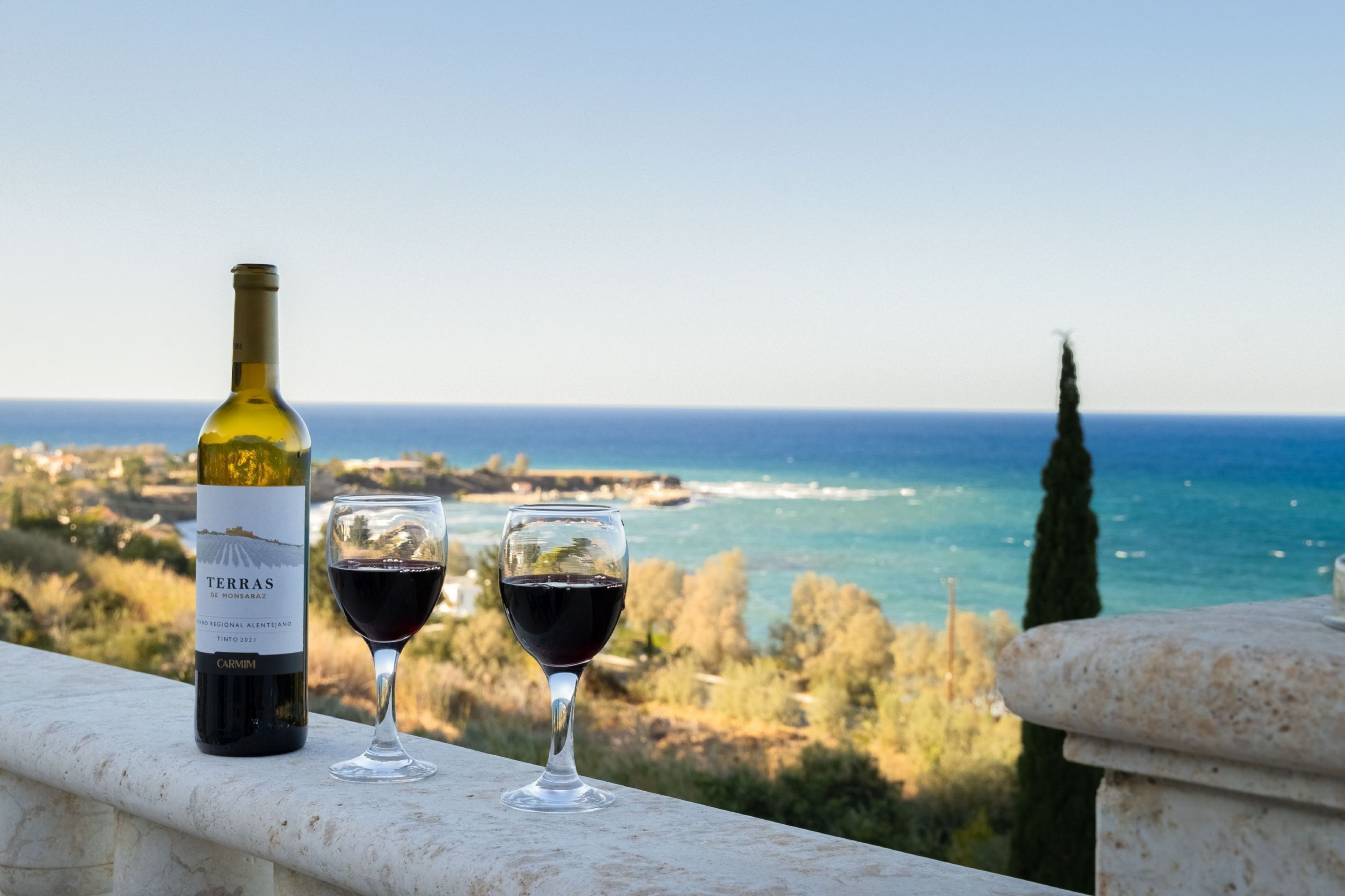 Une bouteille de vin et deux verres sur un balcon donnant sur la mer et le paysage.