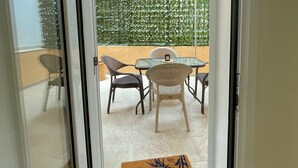 A sliding glass door leading to an outdoor patio with a table and chairs, a decorative wall, and a doormat. - Pistachio Suite - Town Centre (Kerkira)