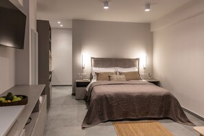 Une chambre moderne avec un grand lit, des tables de chevet, un téléviseur à écran plat et une petite table d’appoint avec une lampe.