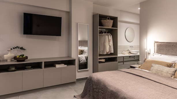 A modern bedroom with a large bed, built-in wardrobe, and a flat-screen TV mounted on the wall. - Iris - By Celestial Suites (Athina)