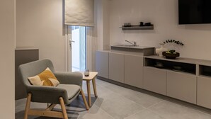 A modern kitchen with a grey armchair, a small table, and a built-in sink. - Iris - By Celestial Suites (Athina)