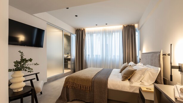 Un dormitorio de hotel moderno con una cama grande, un televisor montado en la pared, una mesita de noche y un escritorio con una silla.
