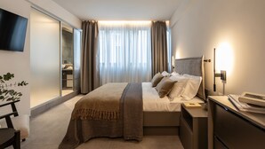 Una habitación de hotel moderna con cama, mesita de noche, lámpara y televisor de pantalla plana montado en la pared.