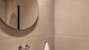 A bathroom with a round mirror, a white sink, and a towel hanging on the wall. - Nyx - by Celestial Suites (Athina)