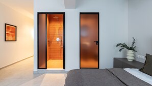 Un dormitorio moderno con una cama, una mesita de noche, un florero con plantas y un acceso corredizo a la zona de la ducha.