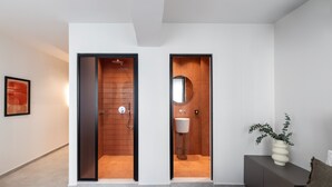 Un dormitorio moderno con una cama, una mesita de noche con un florero y vistas a un baño con ducha y lavamanos.