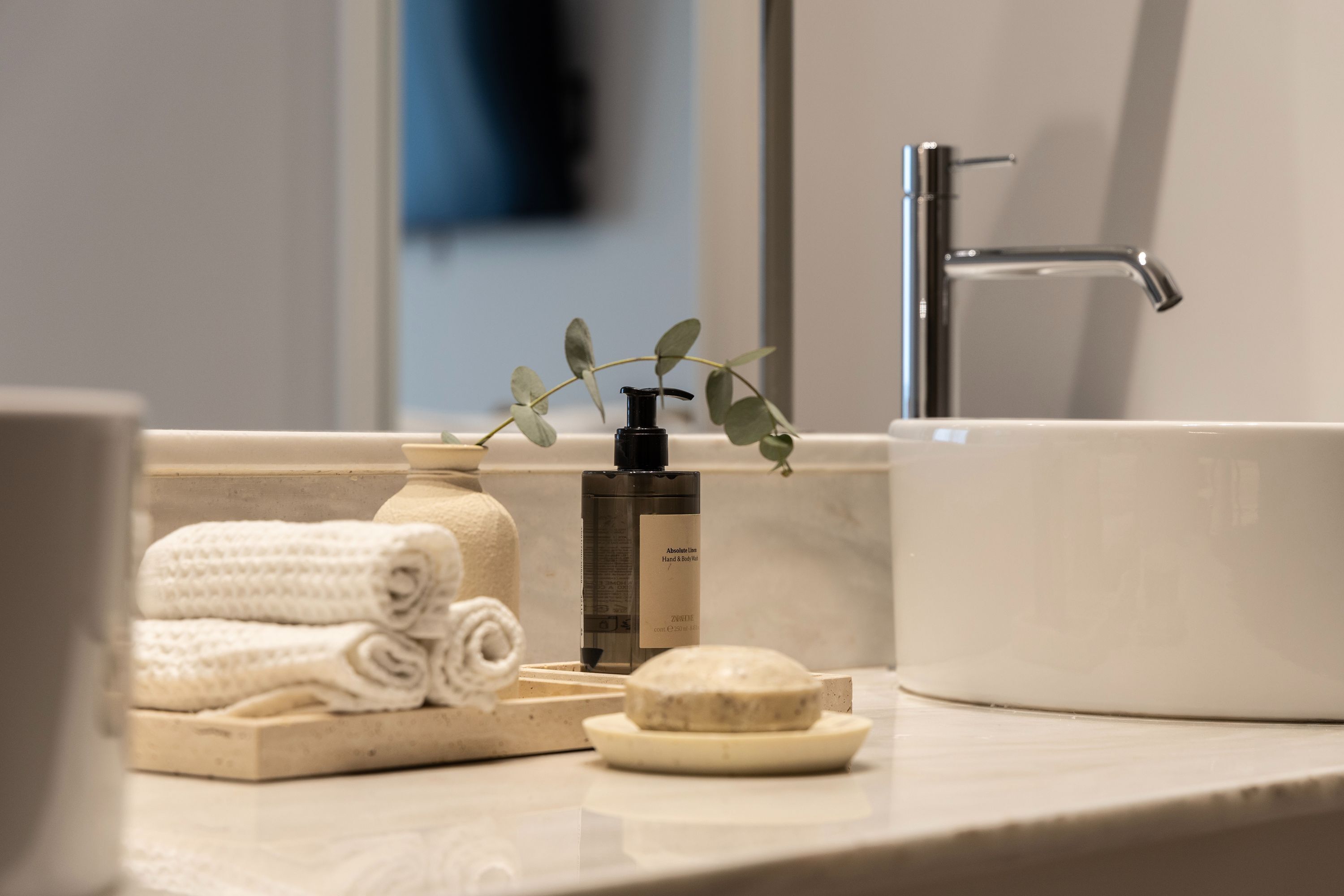 A bathroom with a white sink, a bottle of hand soap, a bar of soap, and neatly folded towels.