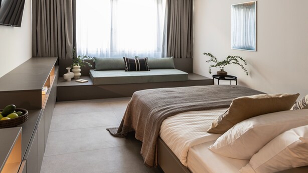 Ein modernes Schlafzimmer mit Bett, Sitzecke, Fernseher und einem Fenster mit Vorhängen.