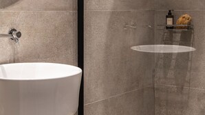 Ein modernes Badezimmer mit einem runden Spiegel, einem weißen Waschbecken und einem Glastregal mit Pflegeprodukten.