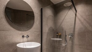 Ein modernes Badezimmer mit rundem Spiegel, Waschbecken in Weiß und einer Duschkabine aus Glas.