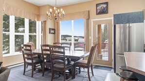 A dining area with a large table, six chairs, a chandelier, and a view of the outdoors. - Fabulous 5-bedroom house at Silver Star Mountain perfect for family getaways! (Vernon)