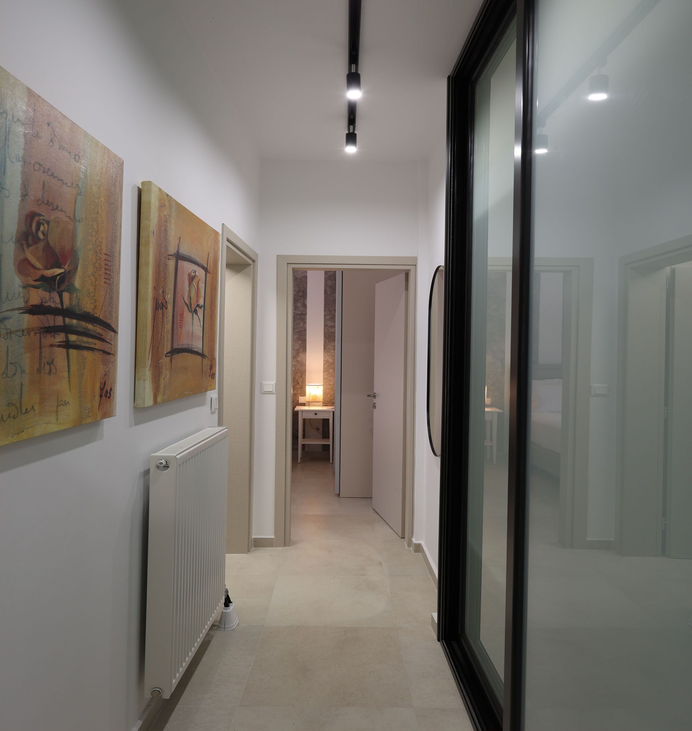 A hallway with artwork on the walls, a radiator, and a door leading to another room.