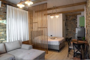 Une pièce comprenant un lit, un canapé, une table à manger avec des chaises, un coin cuisine avec un réfrigérateur et un mur en pierre.