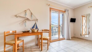 A room with a wooden table, two chairs, a television, and a balcony with a view. - Paxi Apt in Gaios with 1 bedrooms and 1 bathrooms (Gaios)