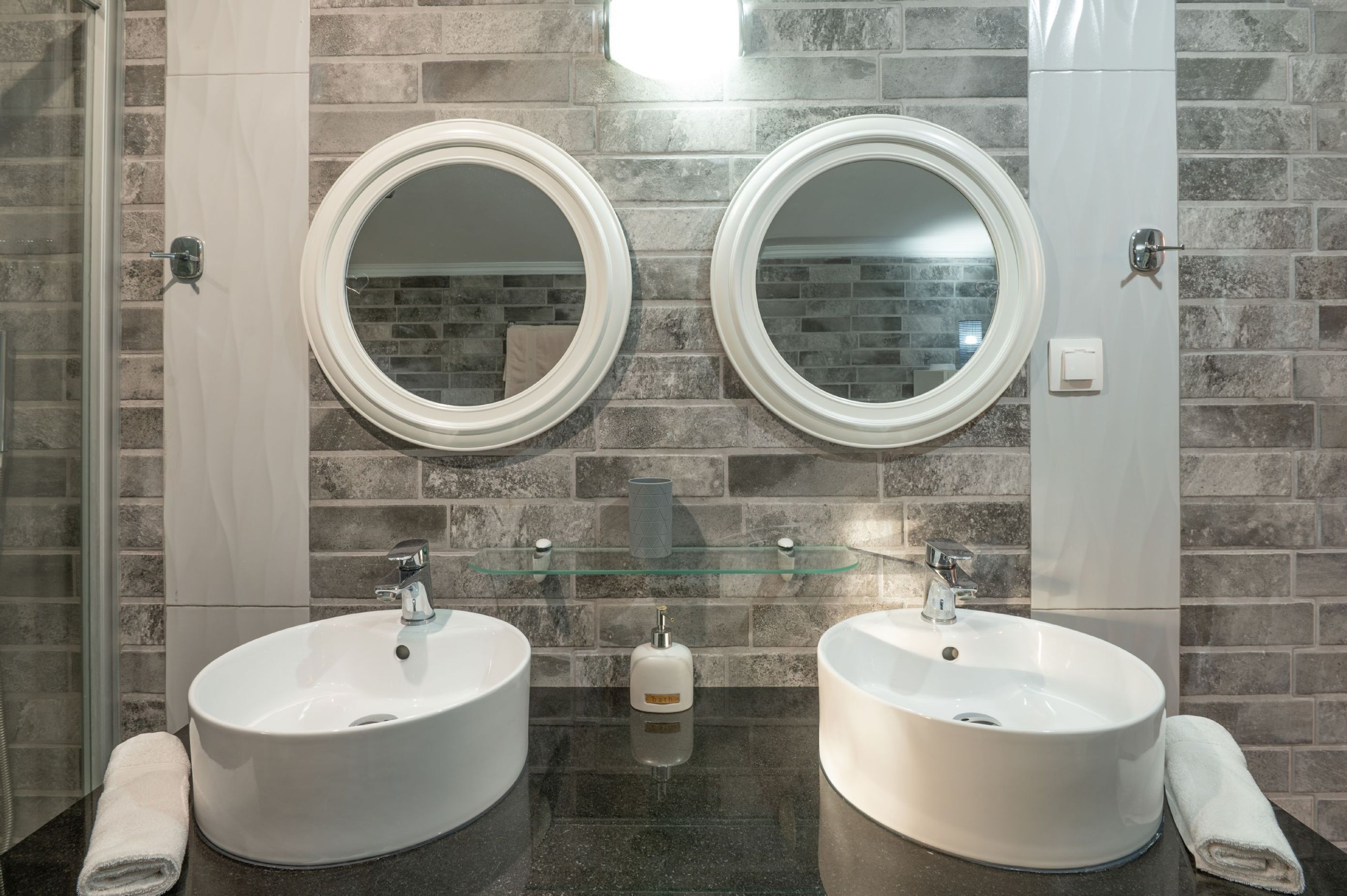 Ein Badezimmer mit zwei Waschbecken, einer Glasablage und einem Spiegel über jedem Waschbecken.