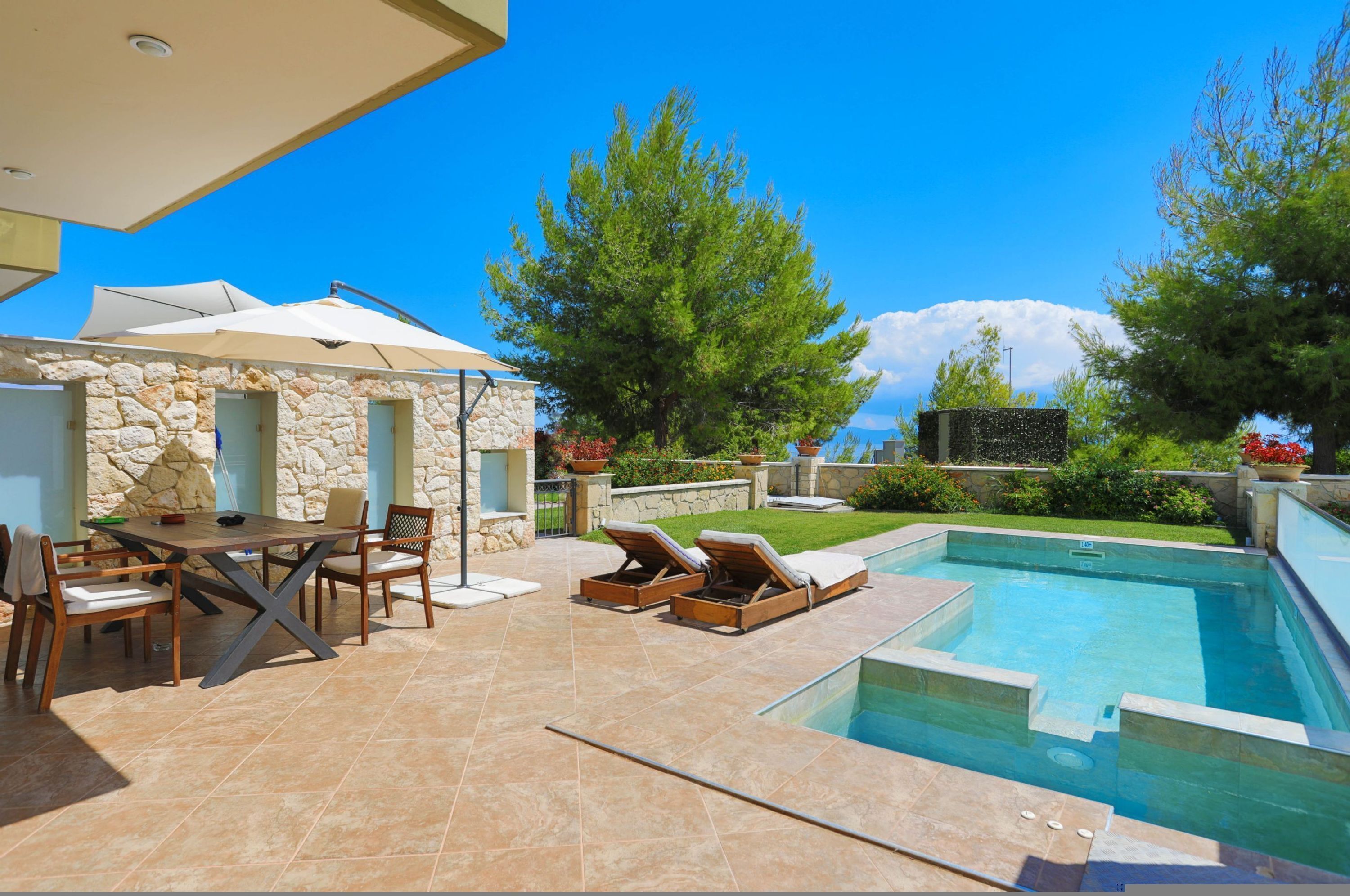 Un espace aménagé au bord de la piscine, avec un mur en pierre, une table entourée de chaises et des chaises longues.