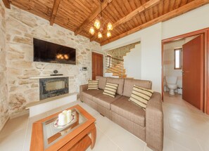 Ein gemütliches Wohnzimmer mit Steinwand, Holzboden, einem Flachbildfernseher, einem Kamin, einer Couch mit Streifen-Kissen und einem Holztisch.