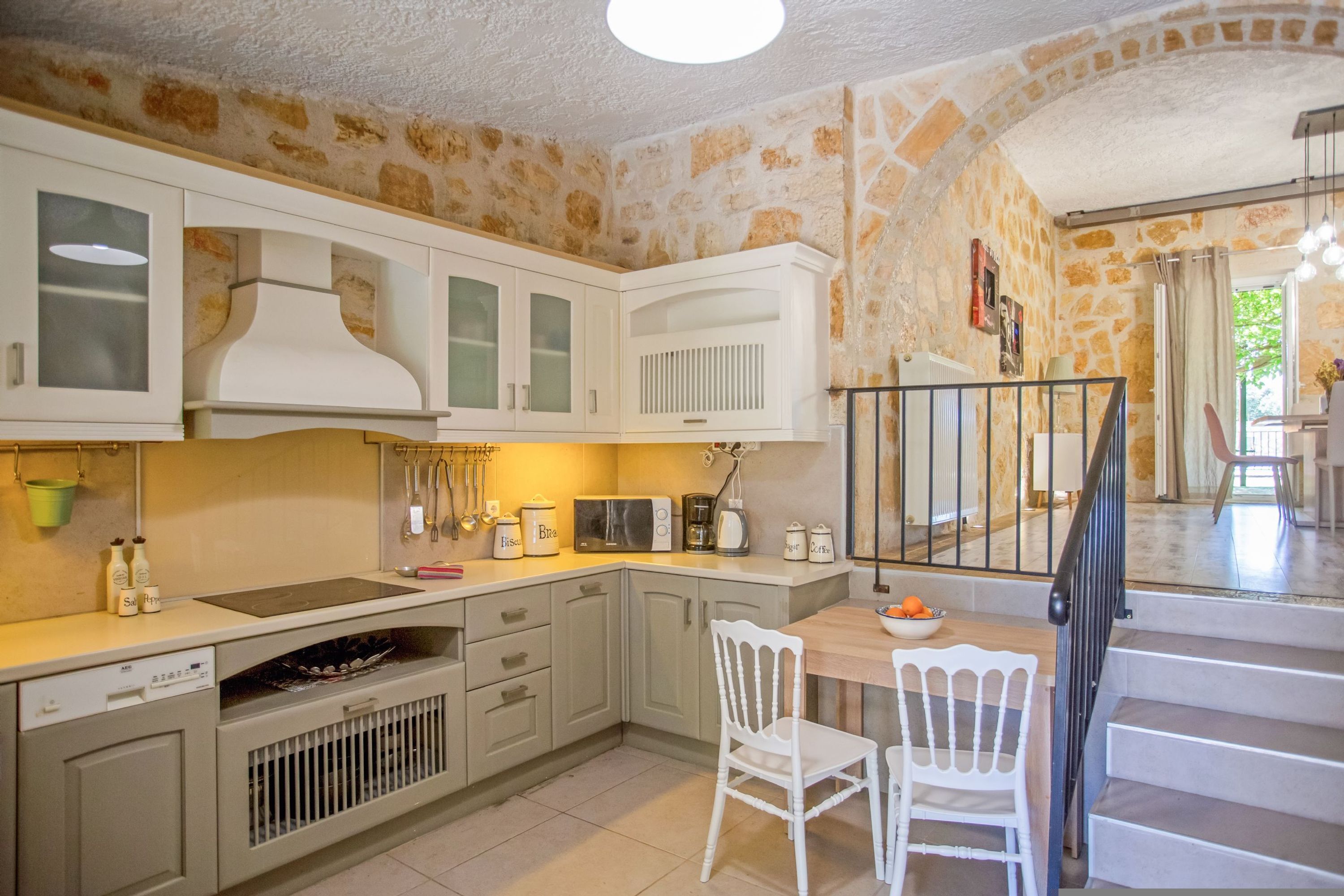 A kitchen with white cabinets, a microwave, and a sink. There is a dining table with chairs and a bowl of fruit.
