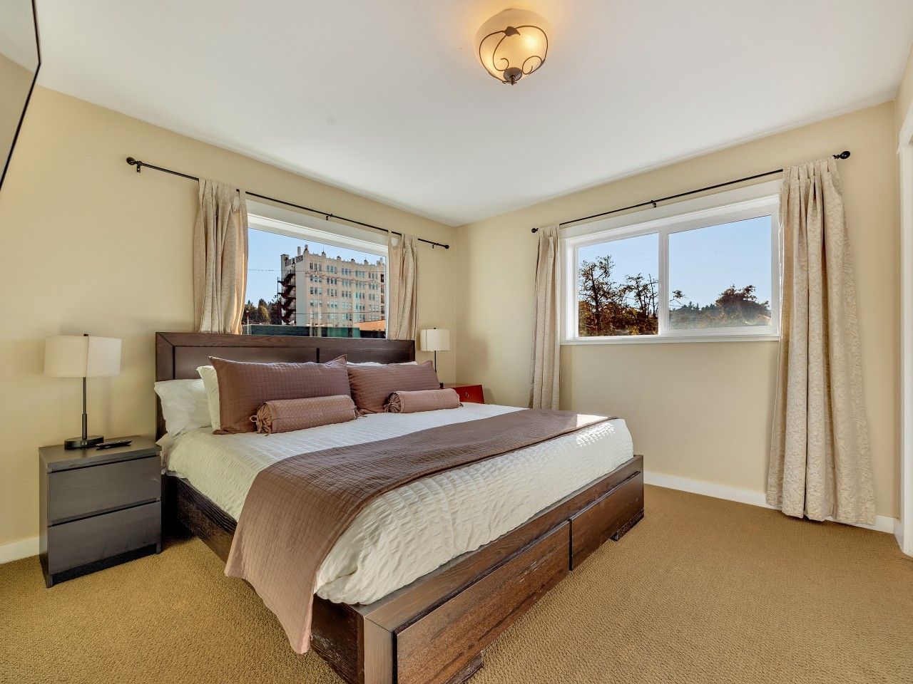 Un dormitorio con cama, mesitas de noche y un ventanal con cortinas.