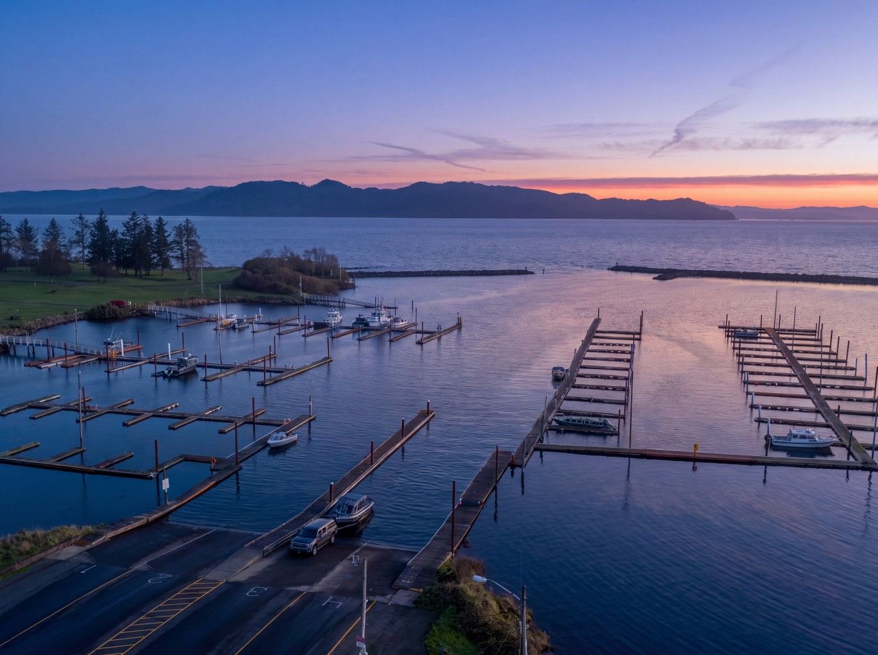A marina with multiple docks and boats, surrounded by water and distant mountains.