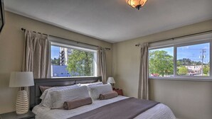 A bedroom with a bed, two bedside tables, two lamps, and large windows with curtains.
