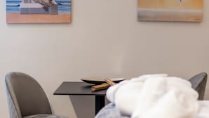 A room with a bed, a table with a bowl and a rolled-up item, two chairs, and two paintings on the wall. - Trikala Mall Suites 2nd Floor Suite Number 21 (Trikala)