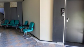 A hotel lobby with teal chairs, a door marked "21", and a tiled floor. - Trikala Mall Suites 2nd Floor Suite Number 21 (Trikala)