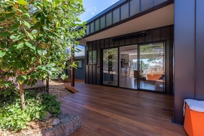 Une maison moderne dotée d’une terrasse en bois, d’une porte vitrée donnant sur la cuisine et offrant une vue sur l’extérieur.