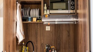 Une cuisine compacte équipée d’un micro-ondes encastré, d’un évier et d’une étagère où sont rangés la vaisselle et les ustensiles de cuisine essentiels.
