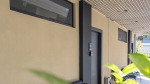Un couloir avec un sol carrelé, des chaises noires, une petite table et une porte portant un numéro.