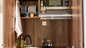 A compact kitchen with a built-in microwave, a sink, and a shelf with dishes and kitchen items.