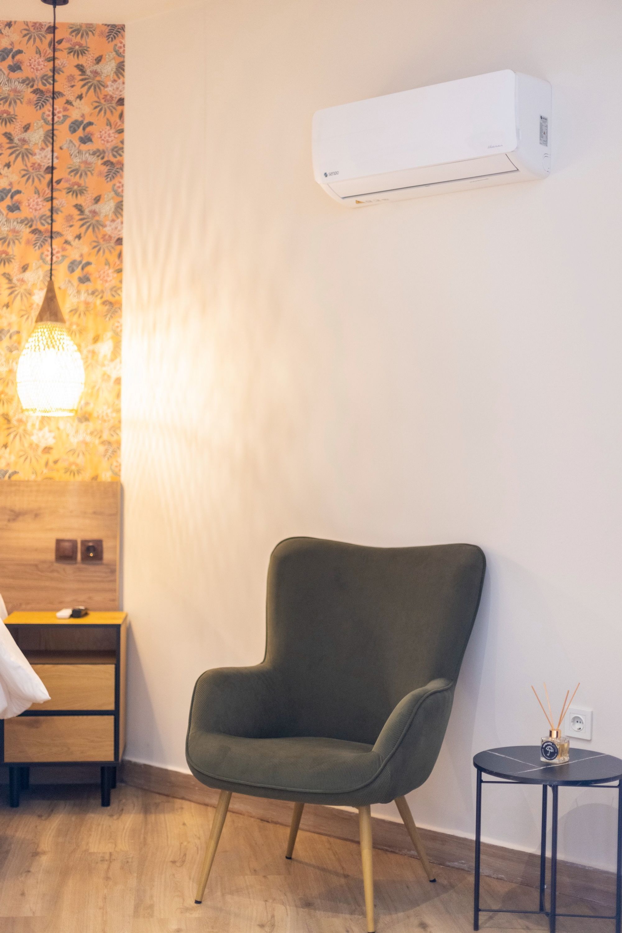 A modern room with a green armchair, a small round table with a candle, and a wall-mounted air conditioner.