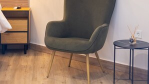 Une chambre moderne avec un fauteuil vert, une petite table ronde ornée d’une bougie et un climatiseur fixé au mur.