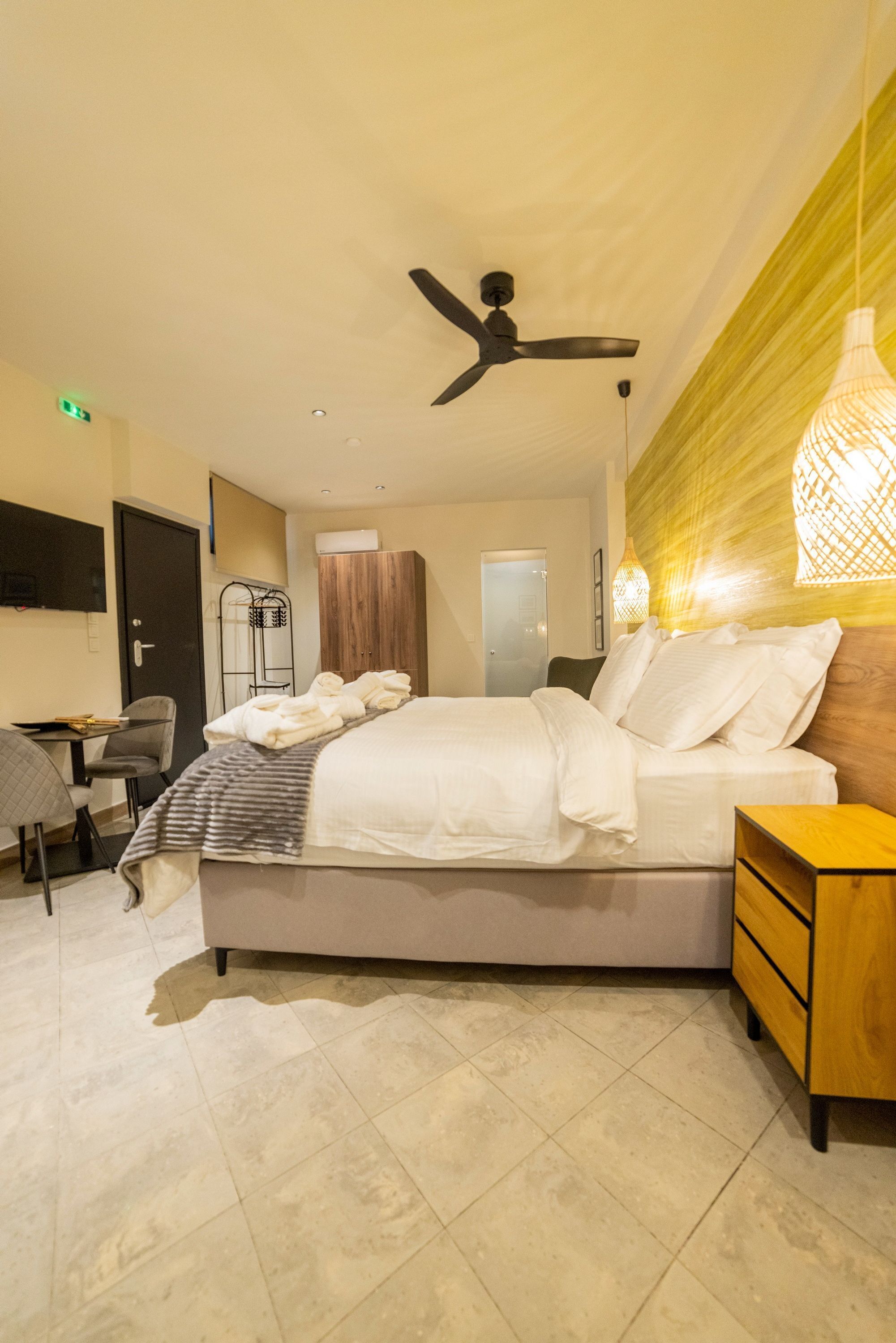 A modern hotel room with a bed, a desk, a chair, a wardrobe, and a ceiling fan.