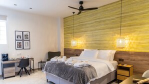 Moderni hotellihuone, jossa on sänky, työpöytä, tuoli ja seinään kiinnitetty kattotuuletin.