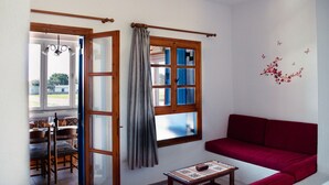 A room with a red sofa, a dining table with chairs, and a window with curtains. - Moonlight Kastraki beach house (Kastraki)