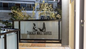 En skylt för Trikala Mall Suites med en modern design, som visar en silhuett av en byggnad och en hästdragen vagn.