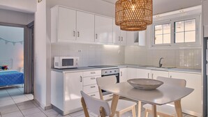 Une cuisine moderne avec des meubles blancs, un four à micro-ondes, une cuisinière et un coin repas agrémenté d’un grand saladier.