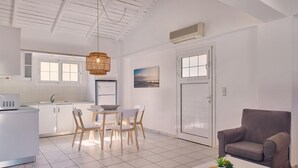 Une cuisine moderne avec des meubles blancs, un coin repas avec une table et des chaises, un canapé gris et une petite table agrémentée de plantes.